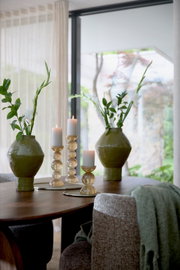 Schuin vooraanzicht van een sfeervol gedekte houten eettafel met groene keramieken vazen, witte bloemen en brandende kaarsen op glazen kandelaars.