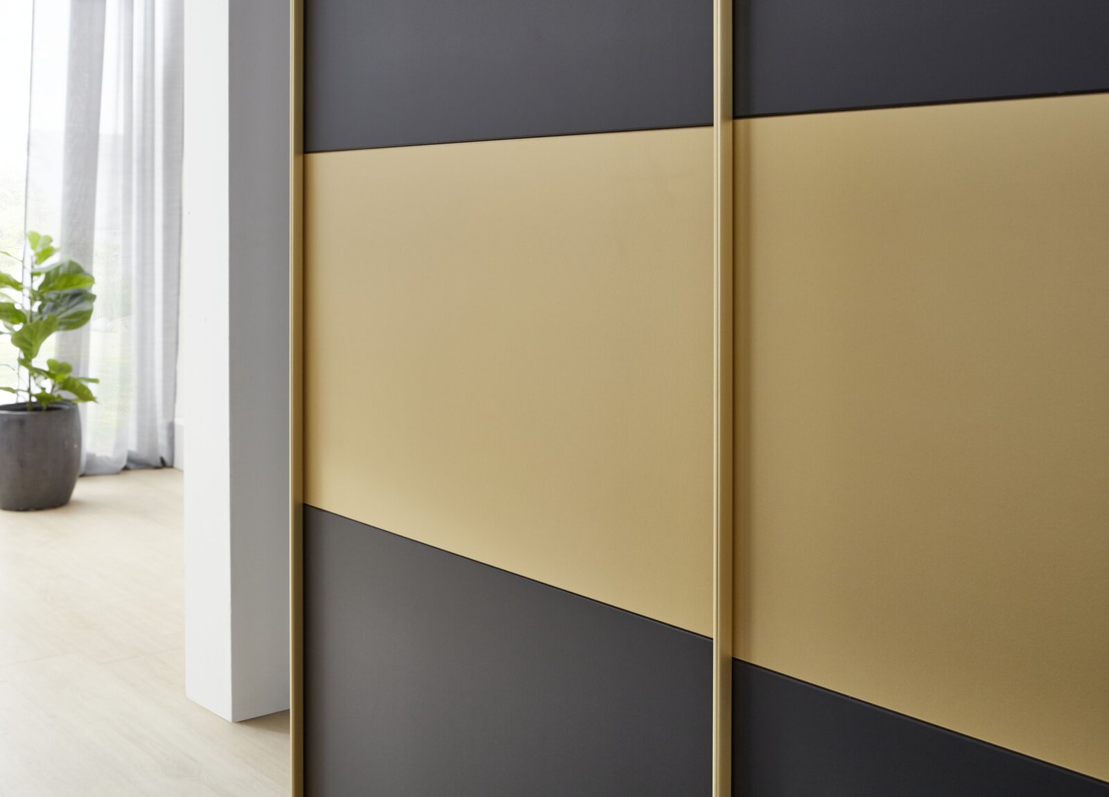Nahaufnahme eines Schwebetürenschranks mit goldenen und schwarzen Paneelen, seitliche Perspektive.
