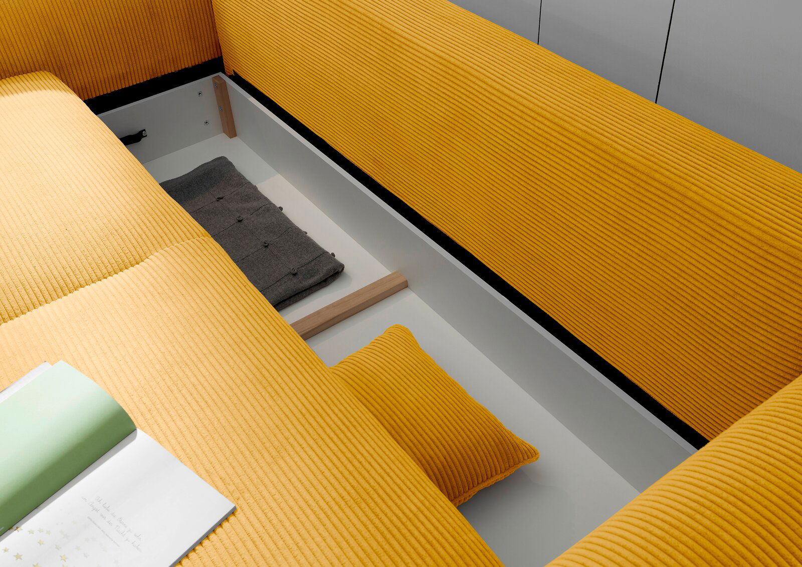 Blick von oben auf ein gelbes Funktionssofa mit Stauraum, in dem ein graues Kissen und ein gelbes Kissen liegen.