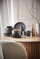 Kombiservice 20-teilig in dunklem Design, bestehend aus Tellern, Schalen und Tassen, auf einem Holztisch arrangiert. Seitliche Perspektive.