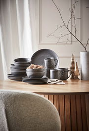 Kombiservice 20-teilig in dunklem Design, bestehend aus Tellern, Schalen und Tassen, auf einem Holztisch arrangiert. Seitliche Perspektive.