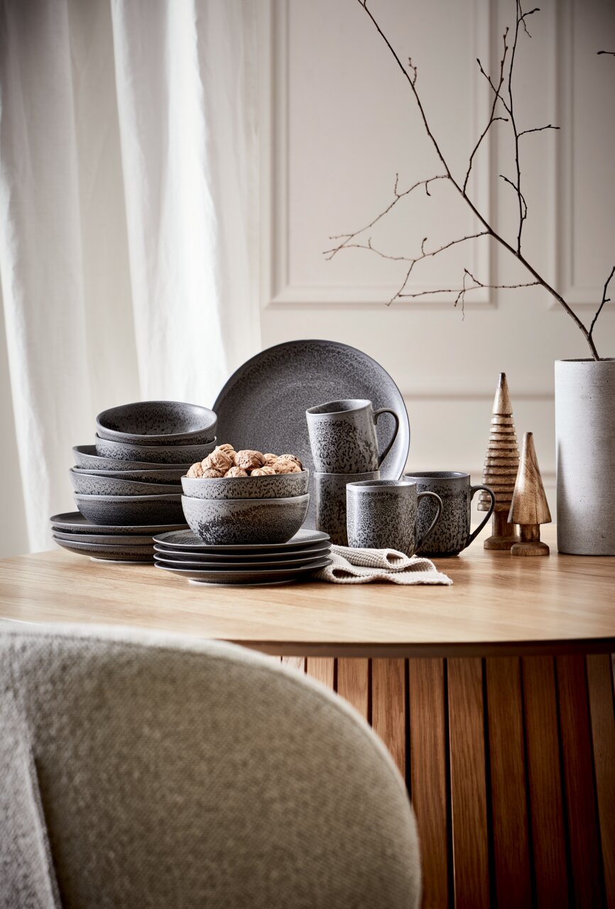 Kombiservice 20-teilig in dunklem Design, bestehend aus Tellern, Schalen und Tassen, auf einem Holztisch arrangiert. Seitliche Perspektive.
