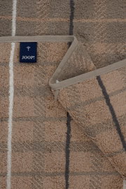 Nahaufnahme aus leicht schräger Draufsicht auf ein JOOP! Frottee-Handtuch in Beige/Taupe mit geometrischem Linienmuster und umlaufender Einfassung