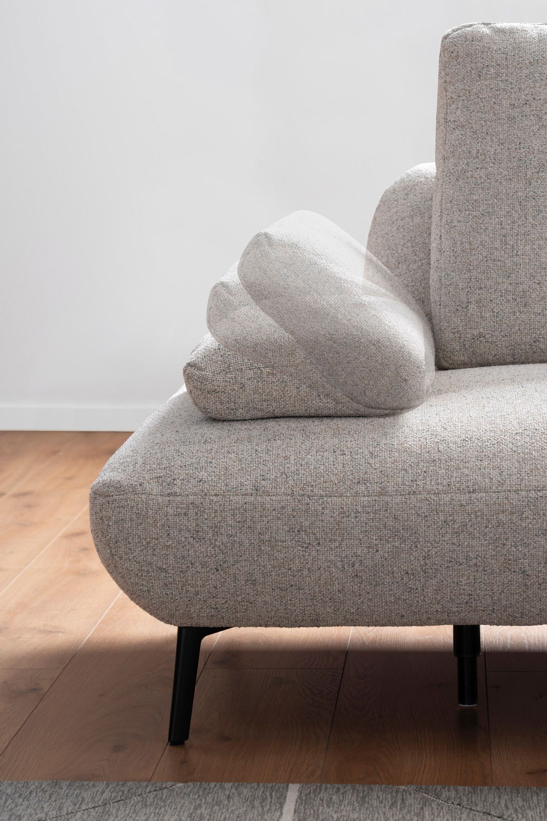 Nahaufnahme einer modernen, grauen Rundecke mit verstellbarer Armlehne, auf einem Holzboden stehend, von der Seite betrachtet.