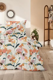 Blumige Bettwäsche mit Aquarell-Blütenmuster in Orange, Rosa und Grün auf weißem Grund, frontal leicht seitlich fotografiert im hellen Schlafzimmer-Setting.