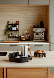 Stijlvolle keukenopstelling met zwarte serveertray met kopjes en zilverkleurige koffiekan op het aanrecht, naast een broodmand en een espressomachine op de achtergrond, gefotografeerd in frontaal perspectief op ooghoogte.