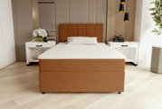 Modernes Boxspringbett in warmem Braun mit gepolstertem, quadratisch gestepptem Kopfteil und weißer Matratze im hellen Schlafzimmer, frontale Ansicht aus leicht erhöhter Perspektive