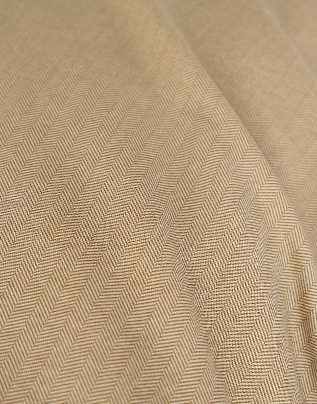 Close-up van beddengoed met visgraatpatroon in beige.