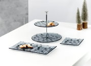 Zweistöckige Etagere und zwei Servierplatten aus grauem Glas mit winterlichem Muster, dekoriert mit Gebäck, aus schräger Vorderansicht