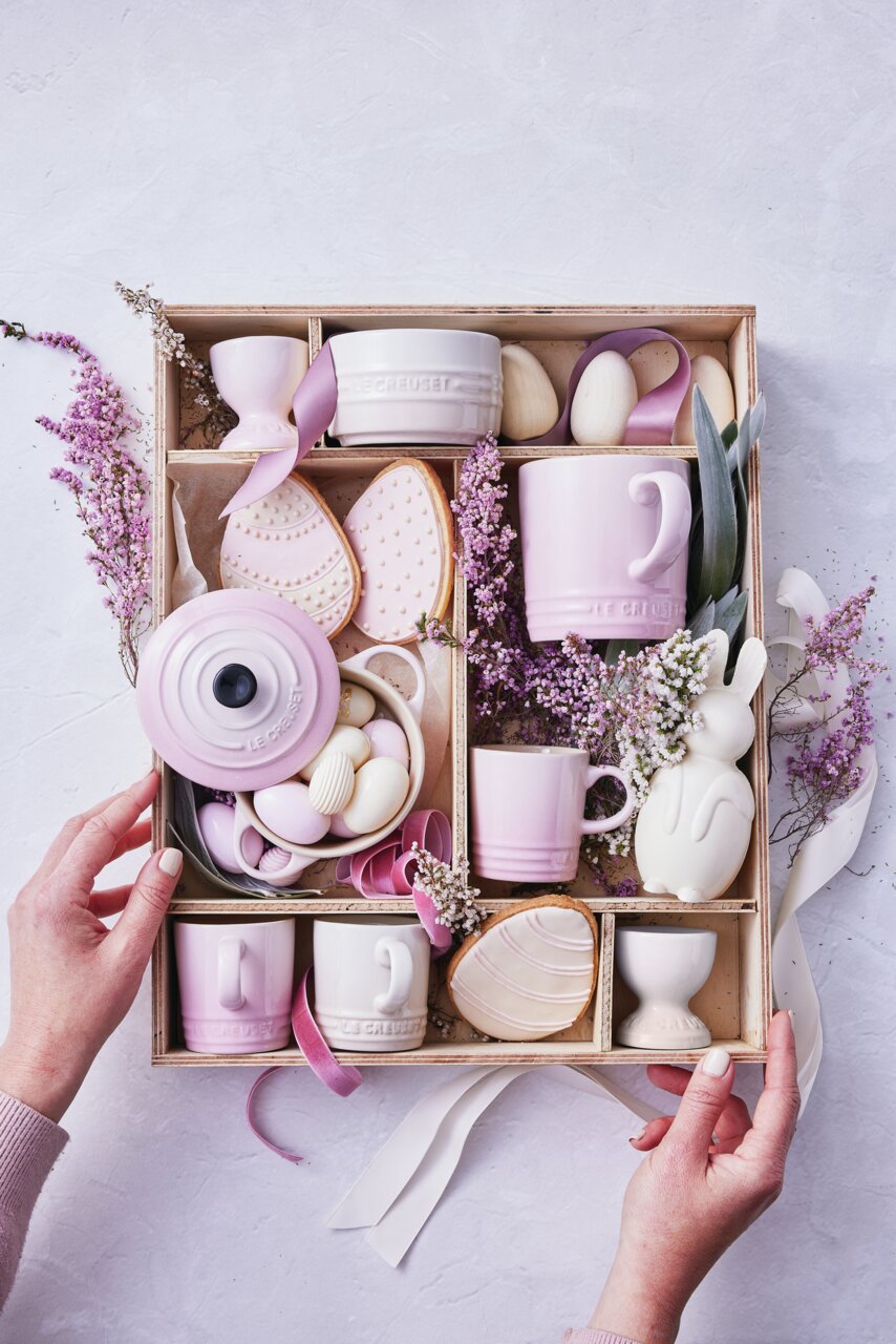 LE CREUSET Kaffeebecher Vogelperspektive auf eine Geschenkbox mit rosa und weißen Bechern, Eiern, Keksen und Dekorationen.