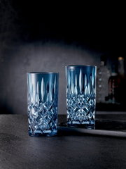 Zwei elegante Longdrinkgläser aus der Noblesse-Serie in blauer Kristalloptik, frontal auf einem dunklen Hintergrund präsentiert.