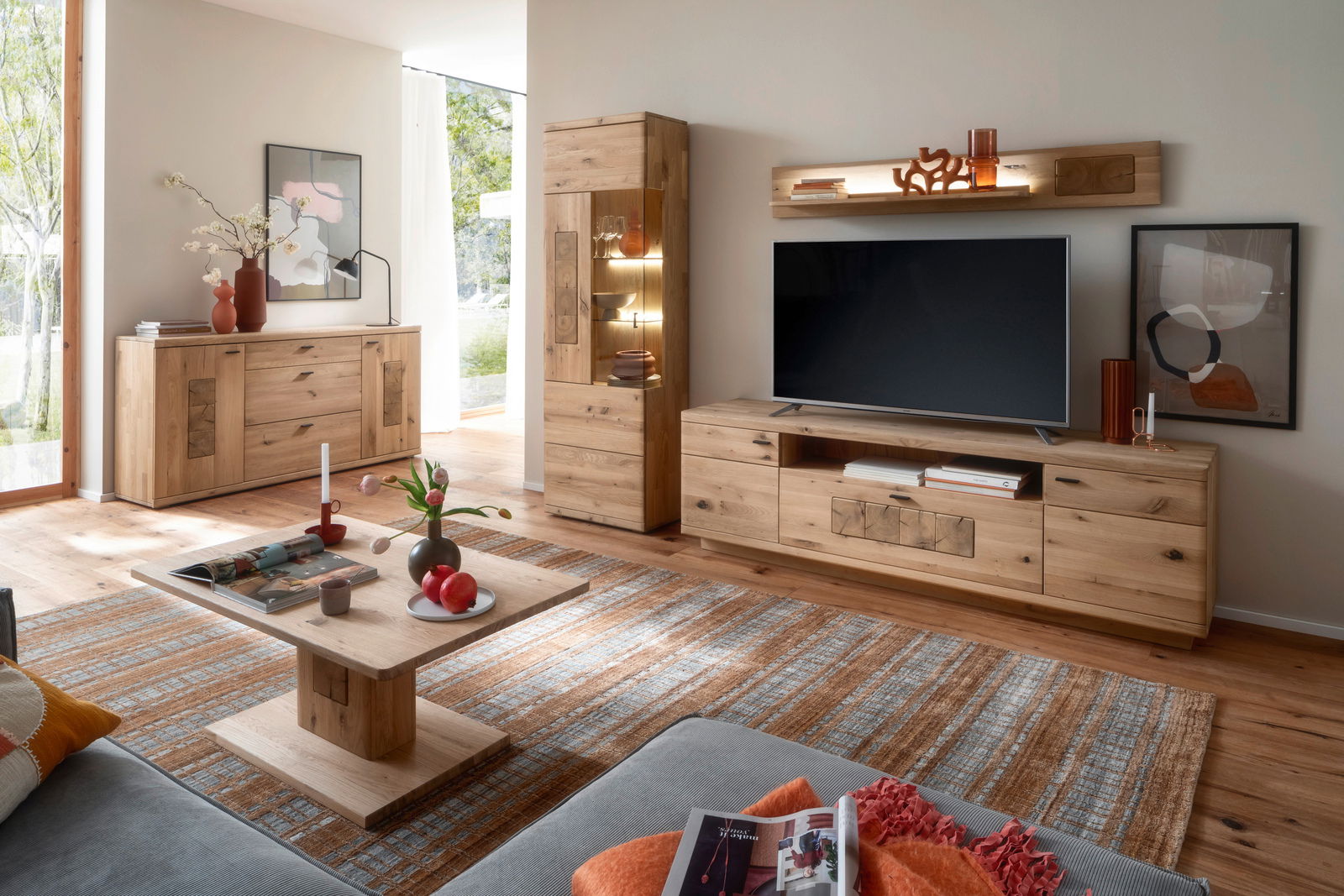 Wohnzimmer mit moderner Holzmöbelkombination, bestehend aus Sideboard, Vitrine, Lowboard und Couchtisch, in einer hellen und gemütlichen Atmosphäre. Perspektive von der Seite.