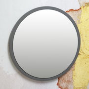 Runder Spiegel mit grauem Rahmen, frontal betrachtet, vor einer kunstvoll gestalteten Wand.
