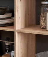 Nahaufnahme einer Kücheninsel mit Holzregalen, gefüllt mit Geschirr, Gewürzen und Vorratsgläsern, seitliche Perspektive.