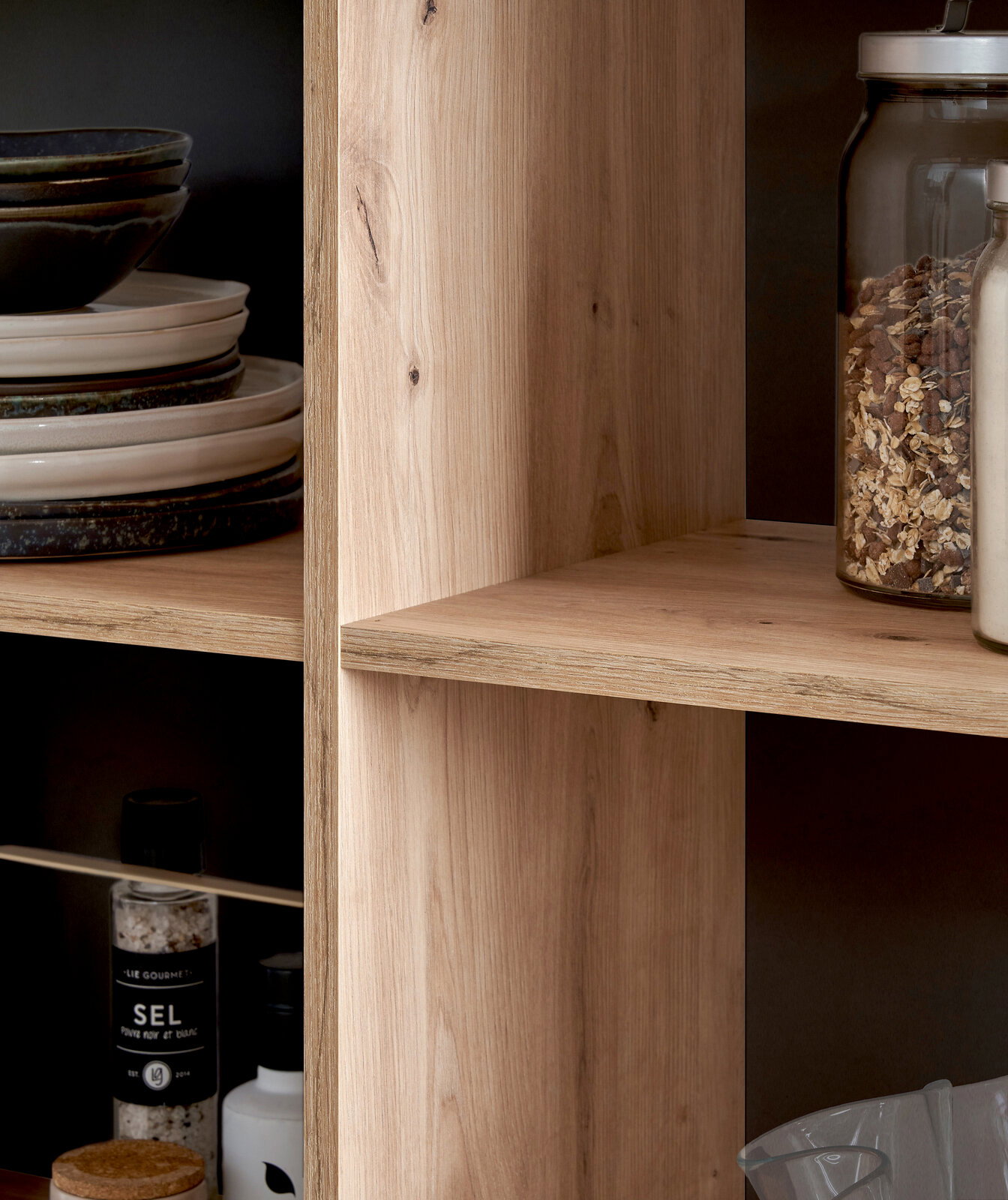 Nahaufnahme einer Kücheninsel mit Holzregalen, gefüllt mit Geschirr, Gewürzen und Vorratsgläsern, seitliche Perspektive.