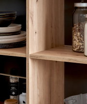 Close-up van een kookeiland met houten planken, gevuld met serviesgoed, kruiden en voorraadpotten, gezien vanuit de zijkant.