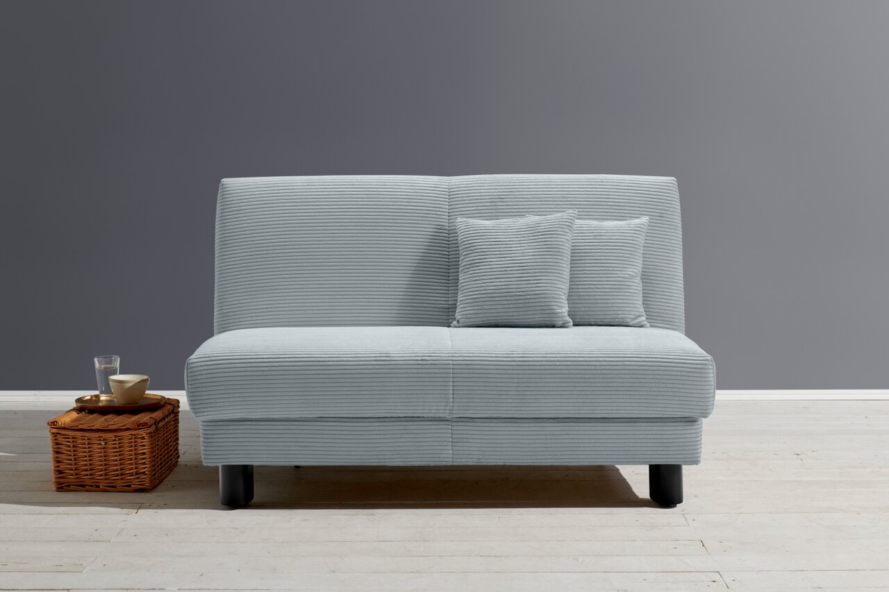 Z2 Schlafsofa ENNY Frontale Ansicht eines grauen Funktionssofas mit zwei passenden Kissen, daneben ein Korb mit einem Glas und einer Schale.
