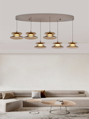 Moderne zevenlichts hanglamp met amberkleurige glazen kappen en warme verlichting, vanuit een licht laag vooraanzicht in een minimalistische woonkamer