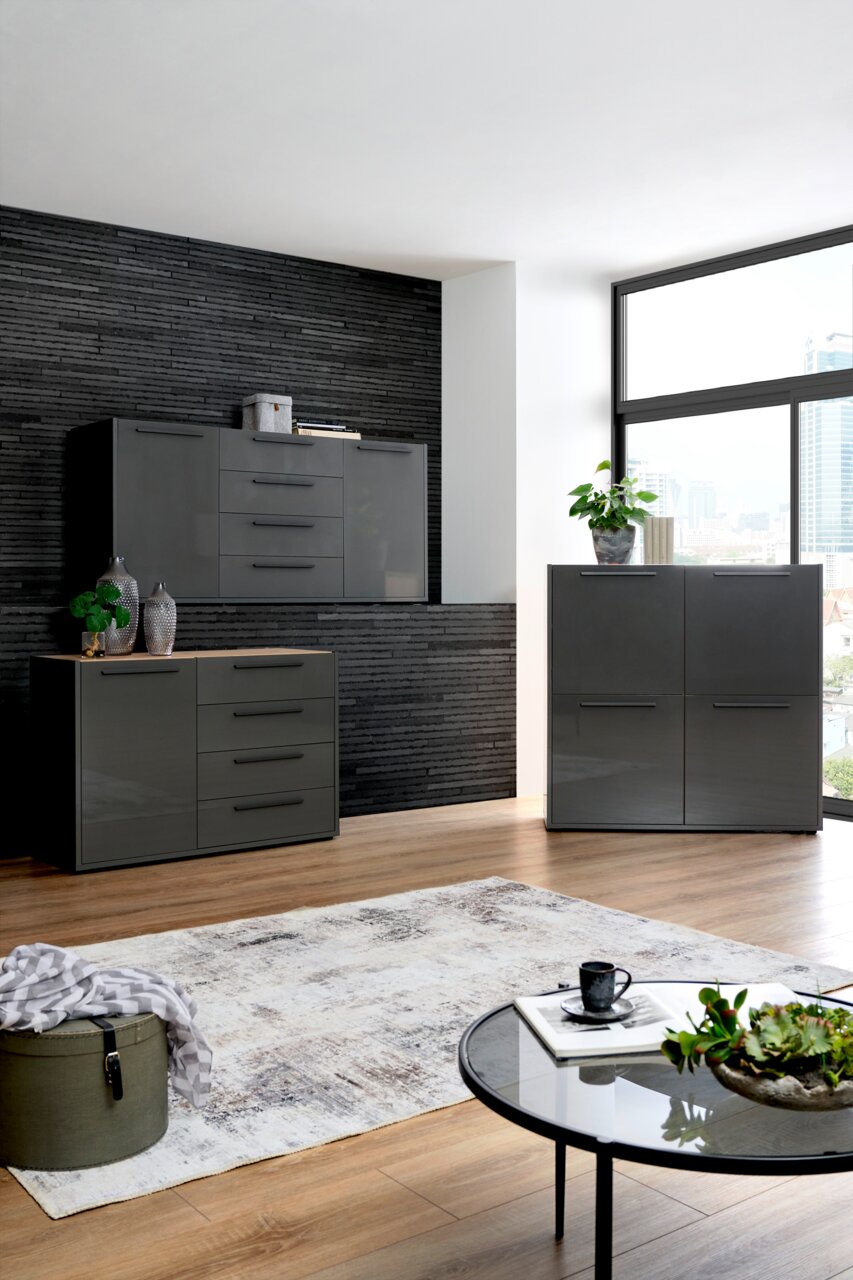 Moderne Wohnzimmermöbel in dunklem Grau, bestehend aus Kommode, Sideboard und Highboard, in einem stilvoll eingerichteten Raum mit Holzfußboden und großen Fenstern. Perspektive von vorne.