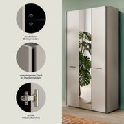Moderner dreitüriger Kleiderschrank in Weiß mit mittlerer Spiegeltür und schwarzen Griffen, im Raum stehend; links Feature-Icons zu verstellbaren Einlegeböden, vorspringender Front und stabilen Metallscharnieren, Ansicht schräg von vorn rechts.
