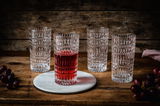 Vier Longdrinkgläser im Ethno-Stil auf einem Holztisch, eines gefüllt mit rotem Getränk, aus frontaler Perspektive.