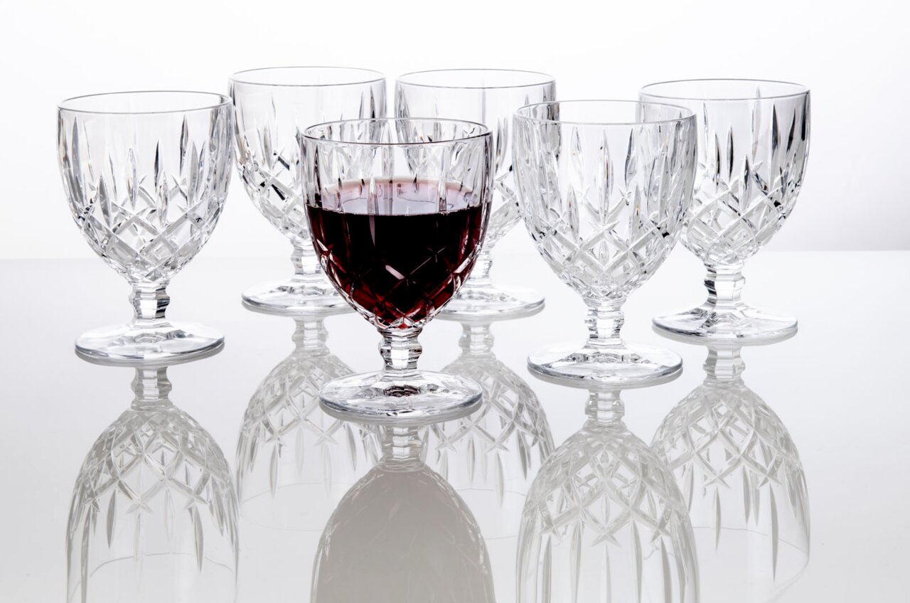 Zes elegante Noblesse-wijnglazen van 350 ml van kristalglas, waarvan één gevuld met rode wijn, op een spiegelend oppervlak, gezien vanuit de zijkant.