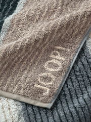 Nahaufnahme eines gestreiften JOOP! Handtuchs in verschiedenen Grautönen mit eingewebtem Logo.