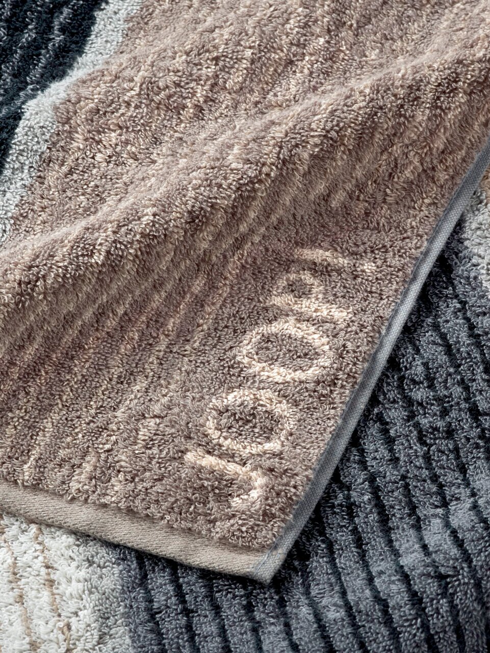 JOOP! Handtuch SIGNATURE Nahaufnahme eines gestreiften JOOP! Handtuchs in verschiedenen Grautönen mit eingewebtem Logo.