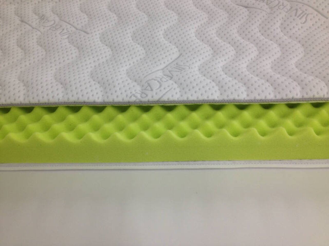 Kaltschaum-Topper SILVERCARE in seitlicher Perspektive, zeigt die wellenförmige Struktur des grünen Schaums und den weißen, gesteppten Bezug.