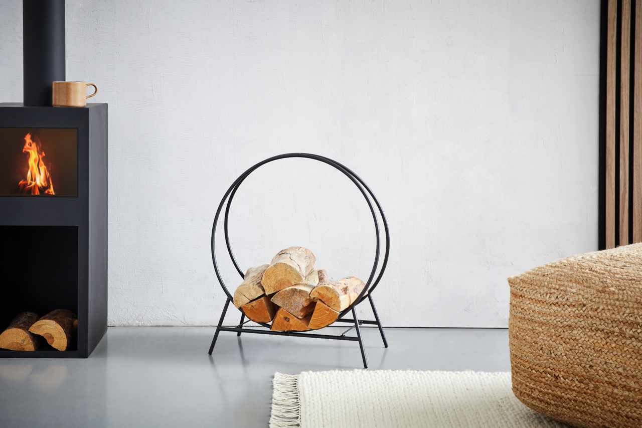 Moderner Kaminholzständer aus schwarzem Metall in einem Wohnzimmer, seitliche Perspektive.