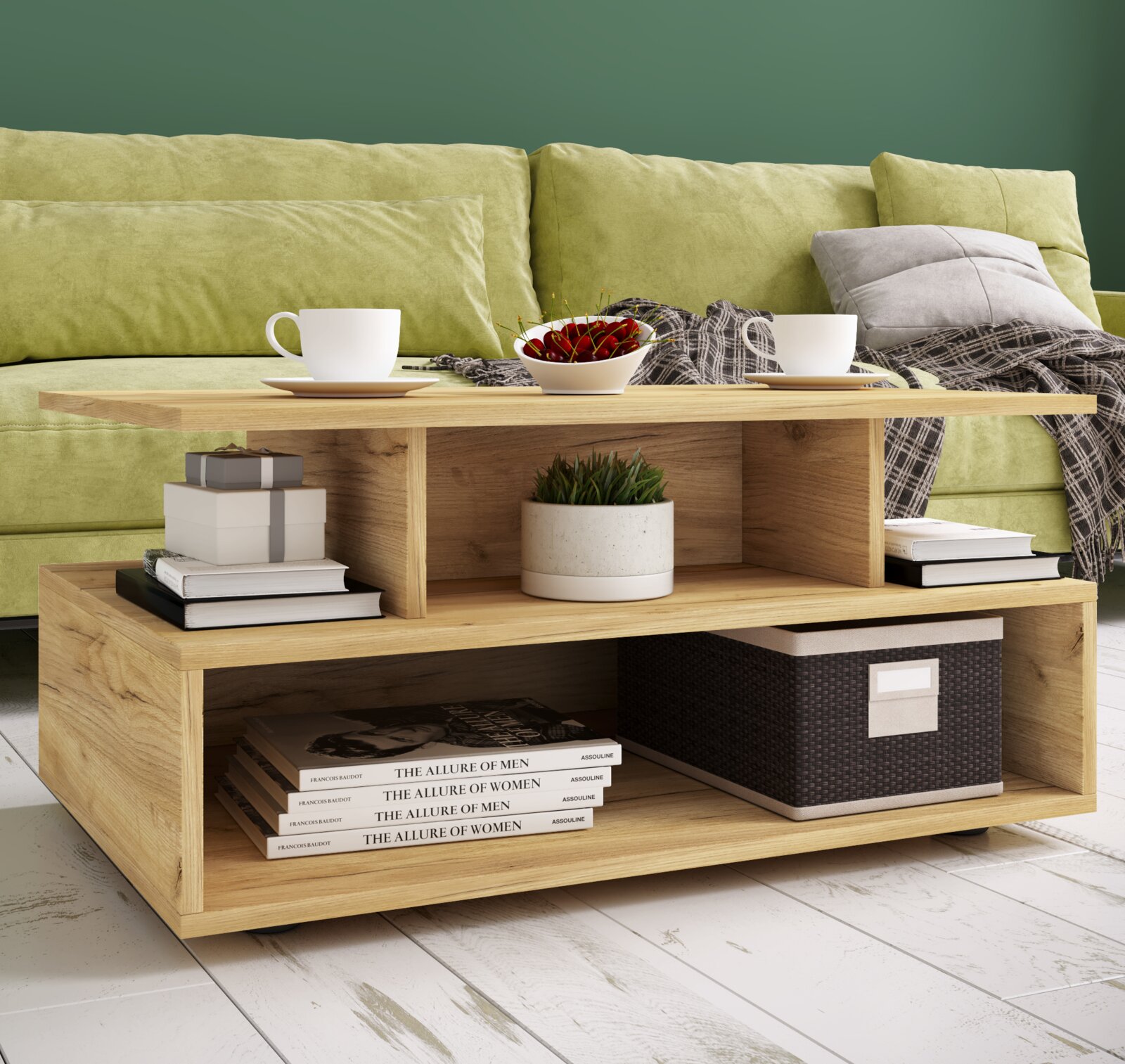 Moderner Couchtisch aus hellem Holz mit offenem Stauraum und Ablagefächern, dekoriert mit Tassen, Schale und Büchern vor grünem Sofa, perspektivisch in leichter Schrägansicht von vorn.