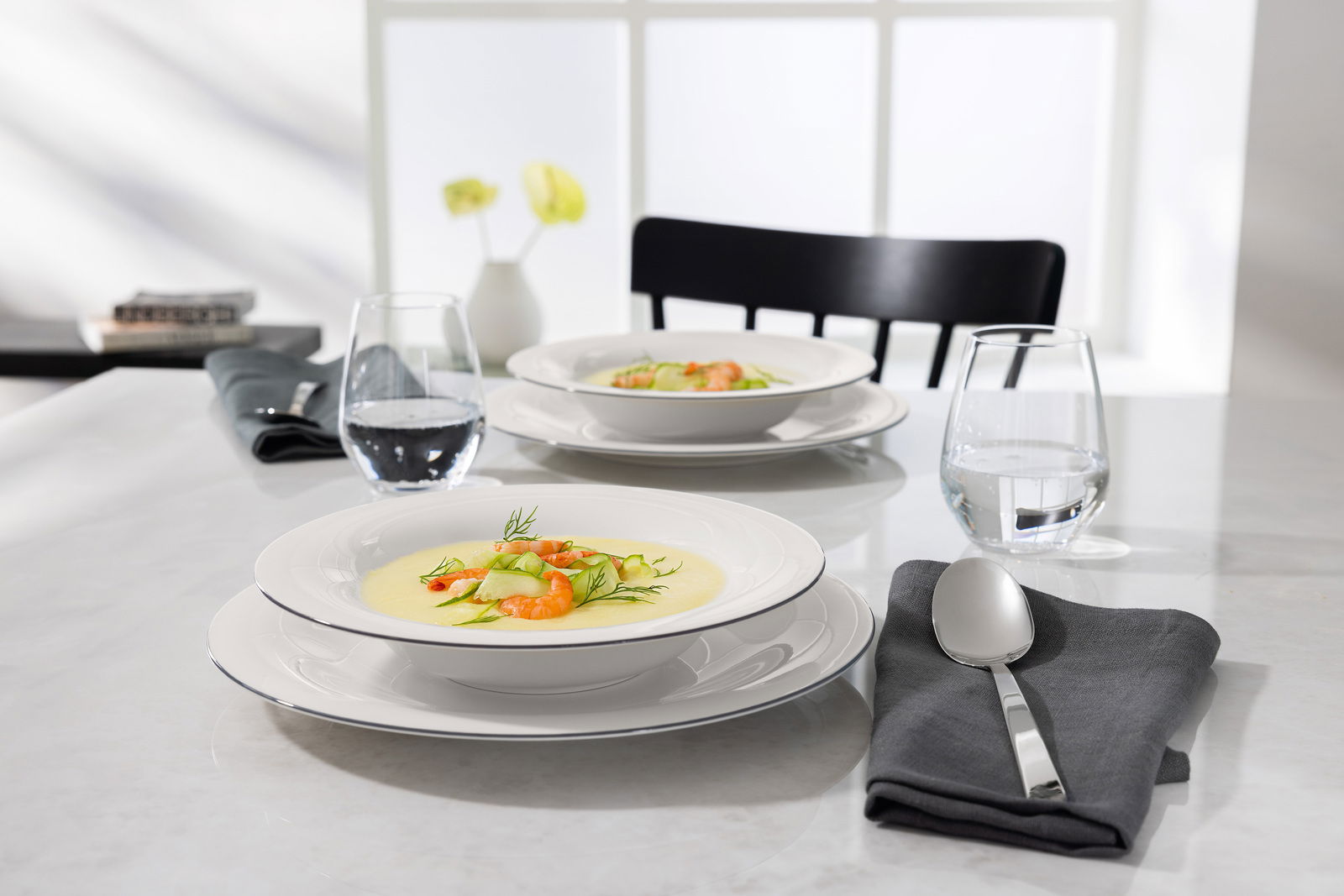 Suppenteller auf einem gedeckten Tisch mit Löffel und Wasserglas, seitliche Perspektive