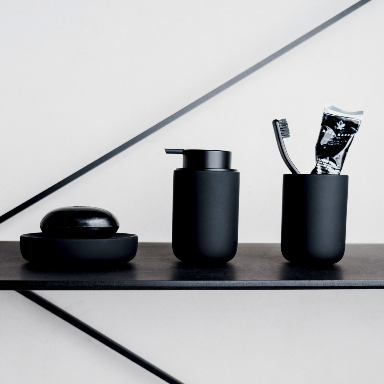 Schwarzes Badezimmer-Set bestehend aus Seifenschale, Seifenspender und Zahnputzbecher mit Zahnbürste und Zahnpasta, seitliche Perspektive.
