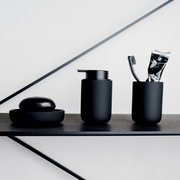 Schwarzes Badezimmer-Set bestehend aus Seifenschale, Seifenspender und Zahnputzbecher mit Zahnbürste und Zahnpasta, seitliche Perspektive.