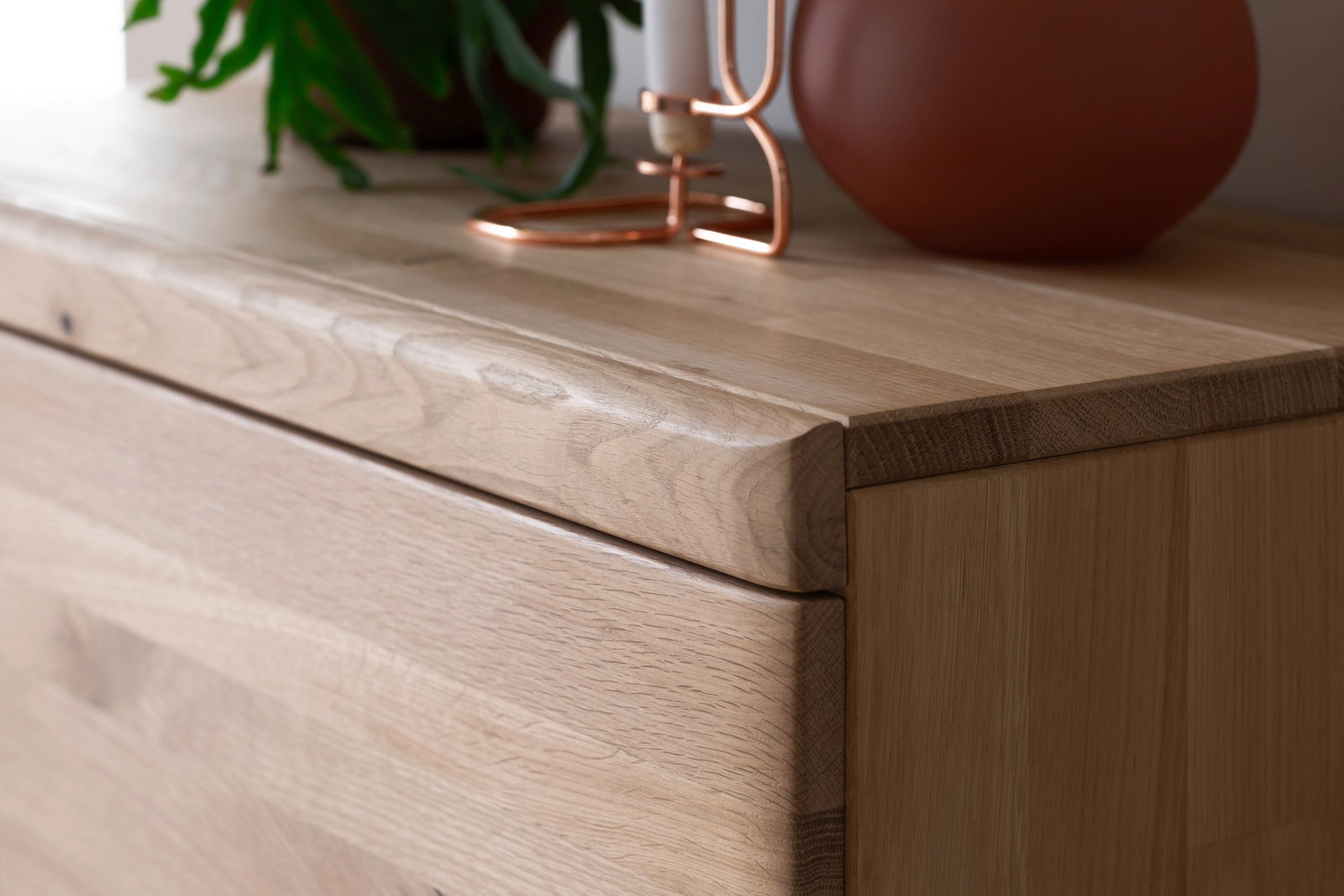 Nahaufnahme eines Holz-Sideboards mit natürlicher Maserung, dekoriert mit einer Pflanze und einem Kerzenhalter. Perspektive von schräg oben.