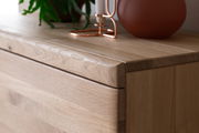 Nahaufnahme eines Holz-Sideboards mit natürlicher Maserung, dekoriert mit einer Pflanze und einem Kerzenhalter. Perspektive von schräg oben.