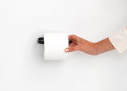Close-up van een moderne, zwarte toiletrolhouder aan de muur, met een hand die er een rol toiletpapier in plaatst.