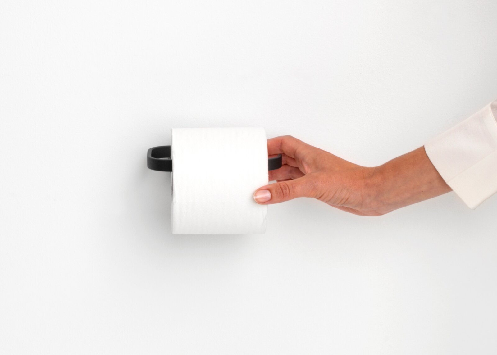 Close-up van een moderne, zwarte toiletrolhouder aan de muur, met een hand die er een rol toiletpapier in plaatst.