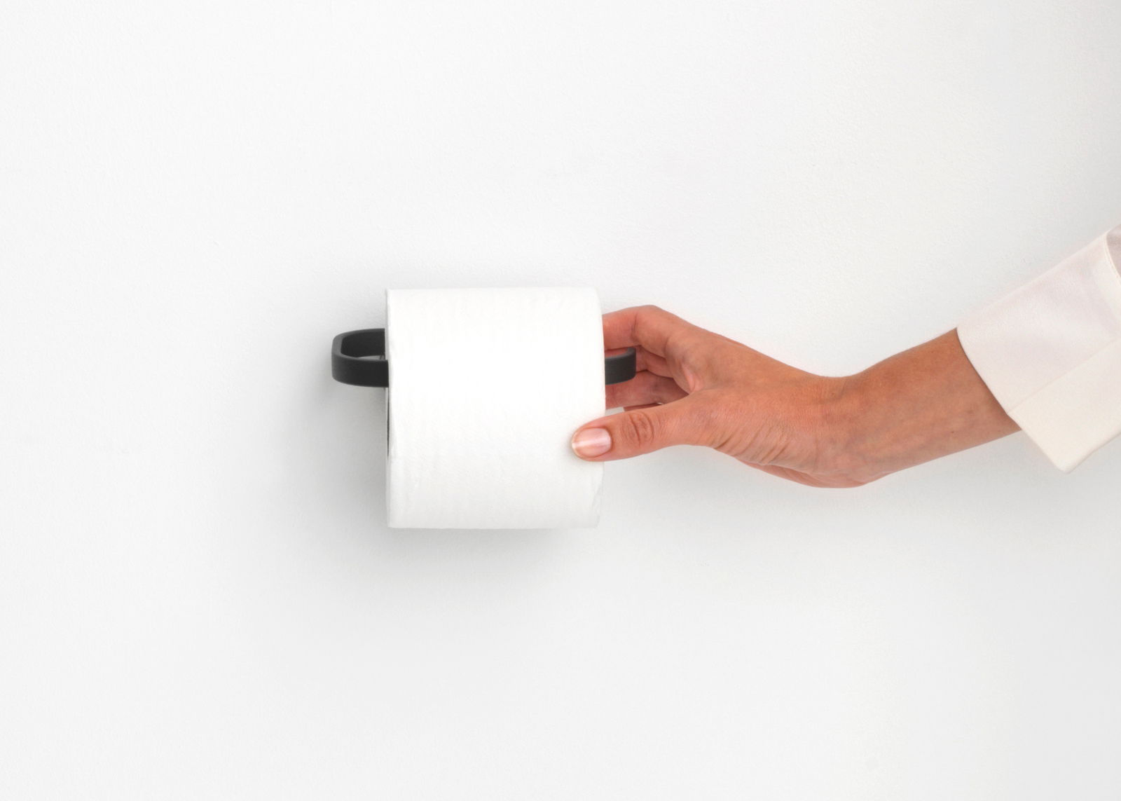 Brabantia Toiletrolhouder MINDSET Nahaufnahme eines modernen, schwarzen Toilettenpapierhalters an der Wand, mit einer Hand, die eine Rolle Toilettenpapier einlegt.