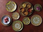 Vogelperspektive auf ein 12-teiliges Tellerset mit Mandala-Muster in lebendigen Farben, arrangiert auf einem Tisch mit Gewürzen und Gemüse.