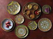 Vogelperspektive auf ein 12-teiliges Tellerset mit Mandala-Muster in lebendigen Farben, arrangiert auf einem Tisch mit Gewürzen und Gemüse.