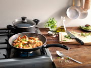 Pfanne mit Garnelen und Kräutern auf einem Herd, seitliche Perspektive