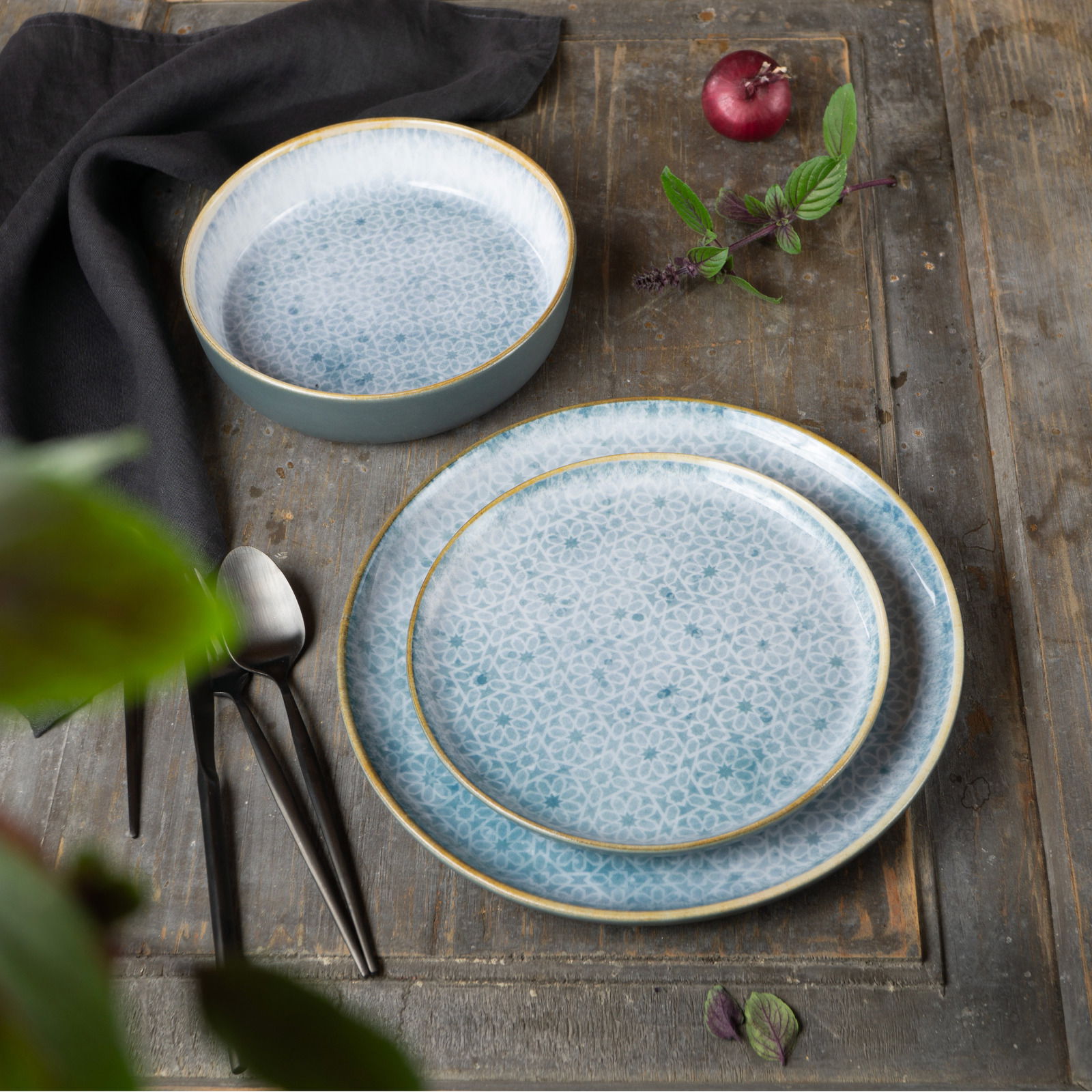 Geschirrset Terra 18-tlg. Azur mit floralem Muster, bestehend aus Tellern und Schalen, auf rustikalem Holztisch von oben fotografiert.