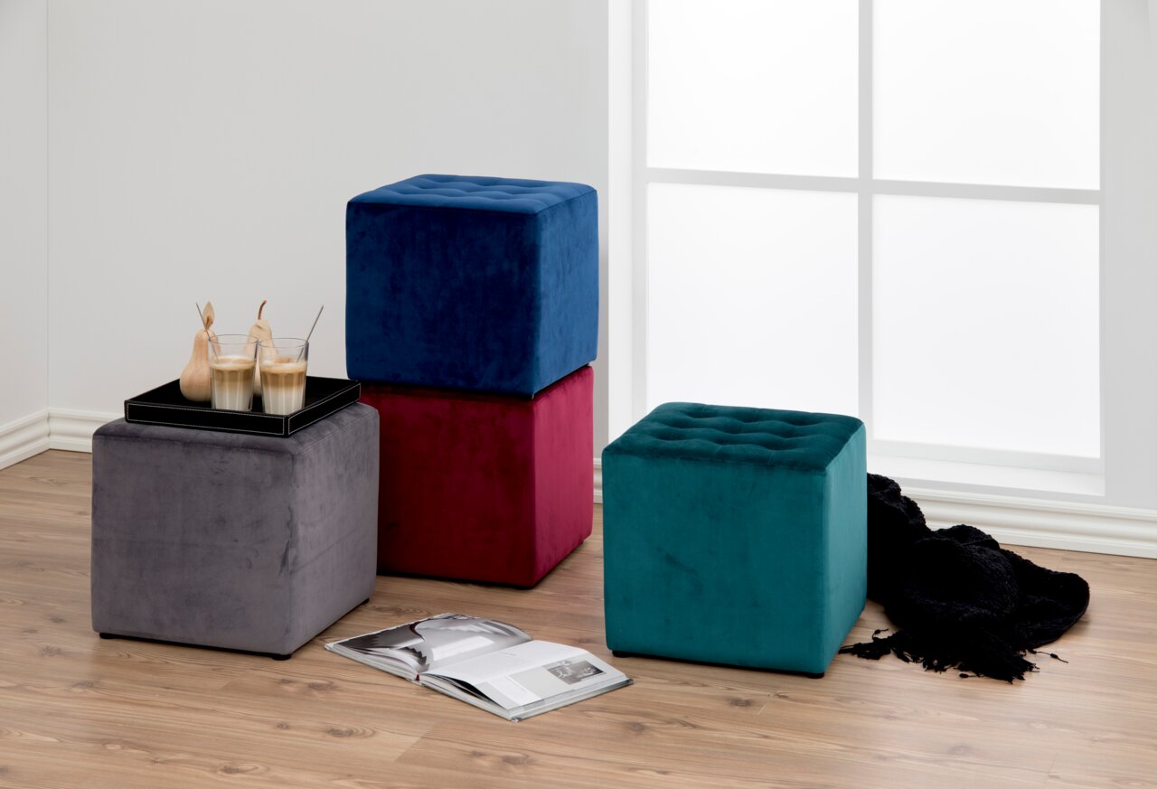 Vier Hocker in verschiedenen Farben, gestapelt und nebeneinander auf einem Holzboden vor einem Fenster. Perspektive von vorne.