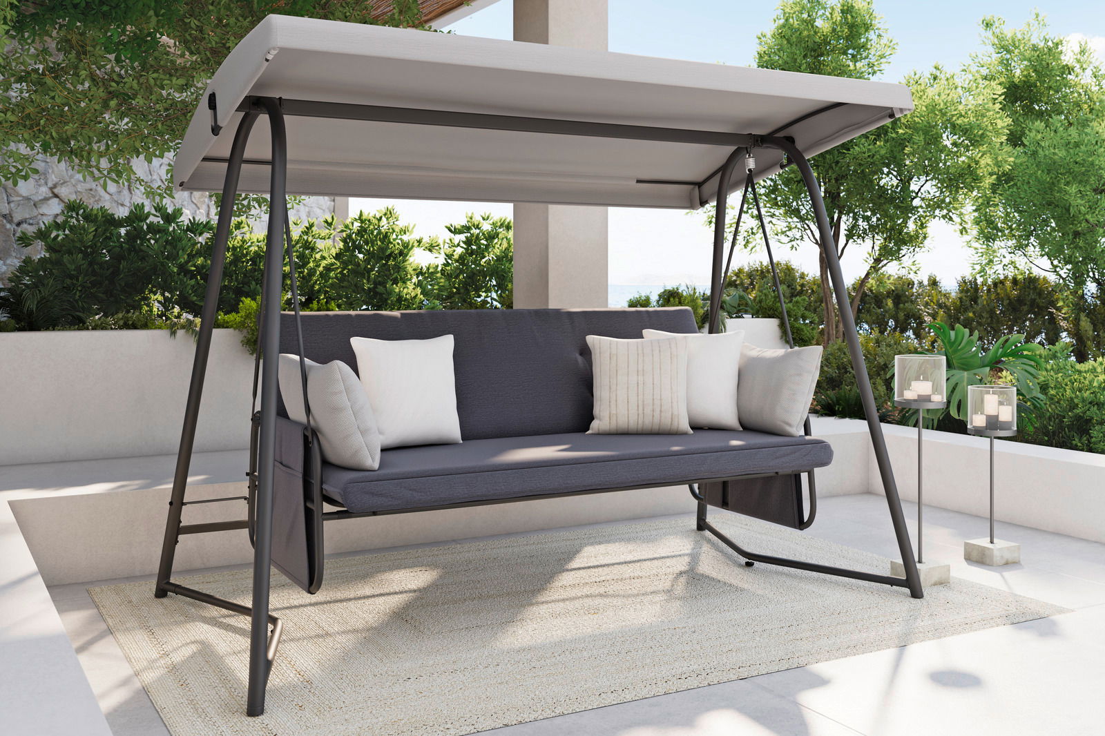 Hollywoodschaukel mit grauem Gestell und Dach, seitliche Perspektive, umgeben von grünen Pflanzen auf einer Terrasse.