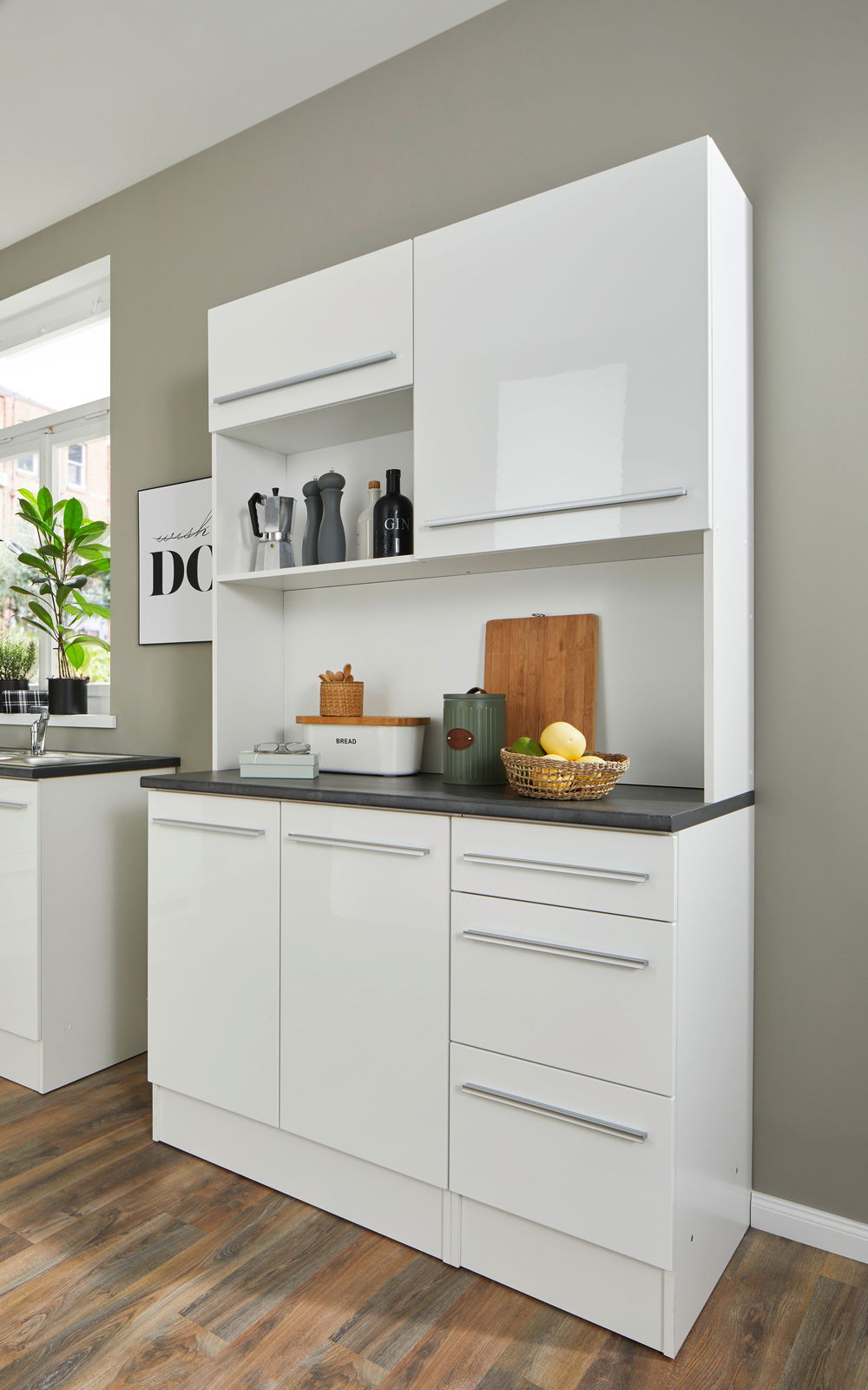 Moderner weißer Buffet-Schrank mit glänzender Oberfläche, mehreren Schubladen und Fächern, gefüllt mit Küchenutensilien, aus seitlicher Perspektive fotografiert.