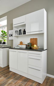 Moderner weißer Buffet-Schrank mit glänzender Oberfläche, mehreren Schubladen und Fächern, gefüllt mit Küchenutensilien, aus seitlicher Perspektive fotografiert.