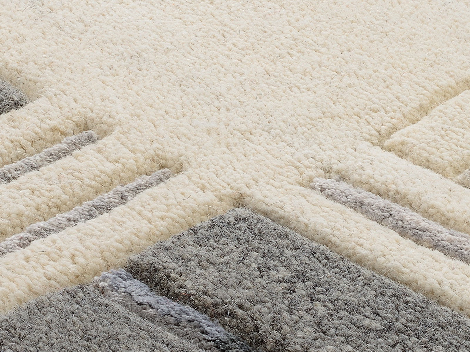 Nahaufnahme eines Wollteppichs mit geometrischem Muster in Creme- und Grautönen, aus seitlicher Perspektive fotografiert.