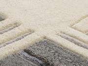 Nahaufnahme eines Wollteppichs mit geometrischem Muster in Creme- und Grautönen, aus seitlicher Perspektive fotografiert.