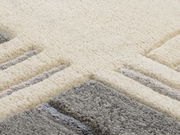 Nahaufnahme eines Wollteppichs mit geometrischem Muster in Creme- und Grautönen, aus seitlicher Perspektive fotografiert.